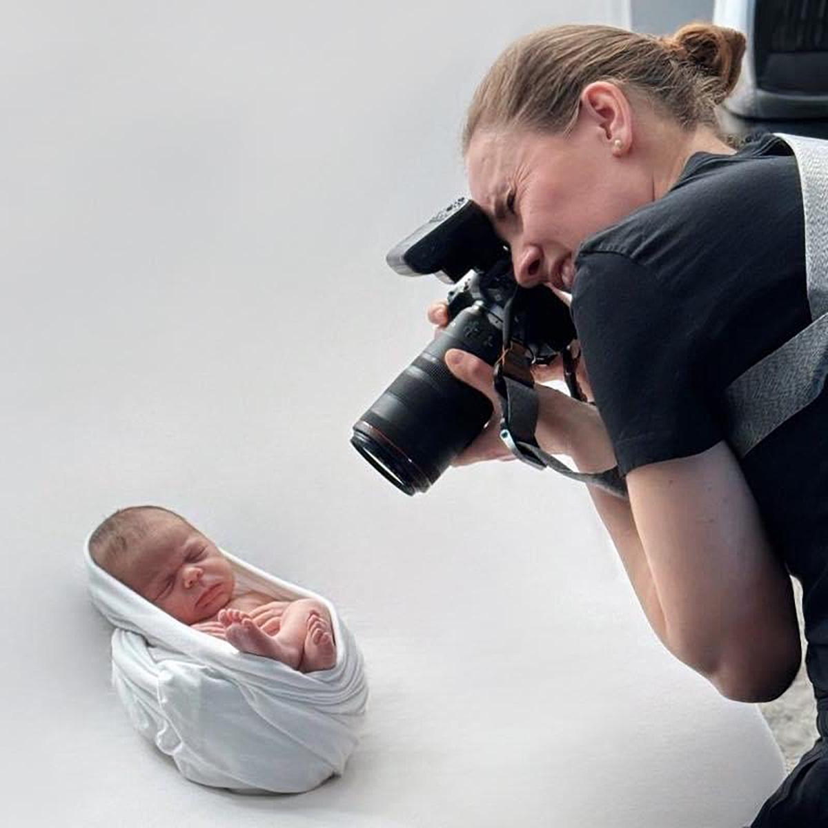 Photographer capturing swaddled newborn on white blanket, behind-the-scenes professional baby photoshoot