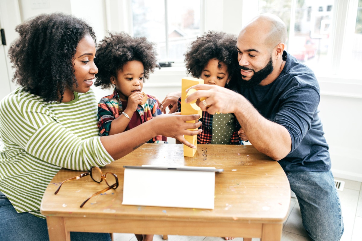 Two parents playing a table game with their twin girls aged 6, engaging in family bonding time.